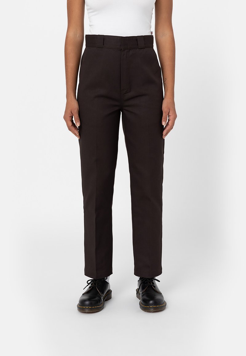 Pantalones marrones de talle alto con un corte ajustado, tejido suave y un ligero brillo. Combinados con zapatos negros de cordones.