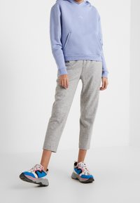 Sudadera de color púrpura claro con un bolsillo frontal, combinada con pantalones de chándal gris ajustados y zapatillas multicolores con acentos en azul, rosa y negro.