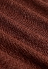 Barna kötött szövet puha textúrával, bordázott mintával és finom árnyalatváltozásokkal a felületen.