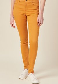 Orange skinny jeans with a smooth texture, high waist, and five-pocket design, paired with white sneakers.
