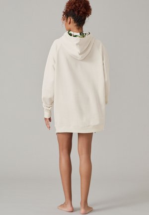 Roomy crèmekleurige hoodie met een kangoeroezak, ribgebreide boorden en een verstelbare capuchon. Heeft een levendige, patroonrijke voering die zichtbaar is bij de hals.