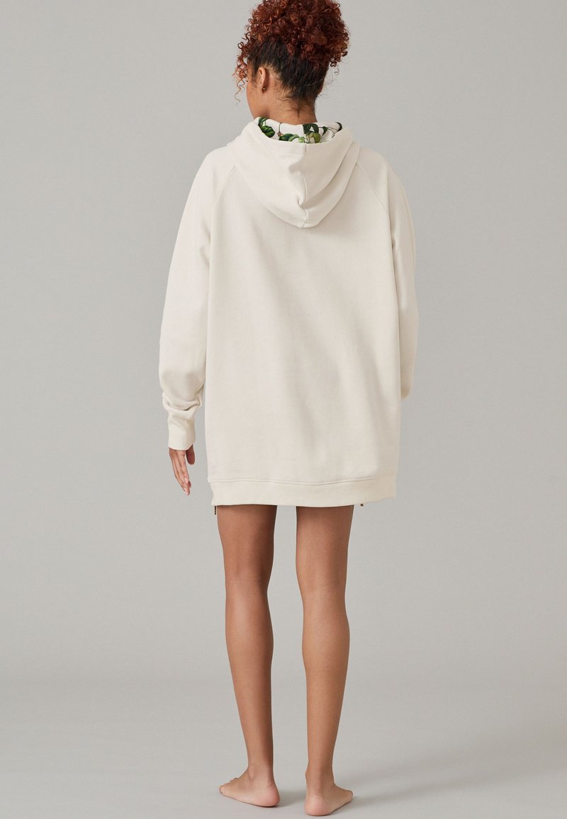 Cremfarbener übergroßer Hoodie mit Kängurutasche, gerippten Manschetten und Kapuze mit Kordelzug. Hat eine lebhafte gemusterte Fütterung, die am Hals sichtbar ist.