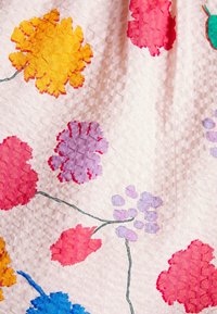 Textiel met een lichtroze achtergrond en gestructureerde bloemenpatronen in geel, rood, roze, paars en blauw, omrand met groene stelen.
