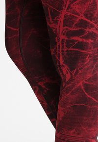 Leggings rossi e neri con un motivo astratto, caratterizzati da una texture liscia e elastica e cuciture piatte per garantire comfort e flessibilità.