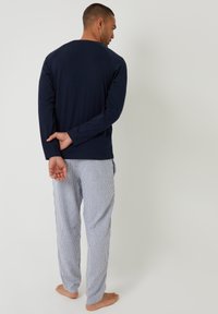 Granatowa bluzka z długim rękawem i okrągłym dekoltem oraz niebieskie i białe pasiaste spodnie od piżamy; miękki materiał, luźny krój, minimalistyczny design, boso.