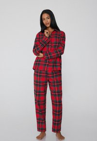 Conjunto de pijama de cuadros rojos hecho de una tela suave; presenta una camisa de botones y pantalones a juego con un clásico patrón de cuadros.