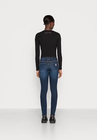 Maglia nera a maniche lunghe e jeans skinny blu scuro con un lavaggio sbiadito, dotati di tasche posteriori e con logo sul collo. Abbinati a scarpe nere.