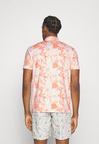 Kratší rukávový triko s květinovým vzorem v odstínech oranžové a růžové, spárované s tečkovanými šortkami zdobenými zelenými kaktusy.