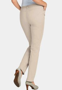 Beige op maat gemaakte broek met een gladde textuur, slanke pasvorm en twee achterzakken, gecombineerd met groene hoge hakken.