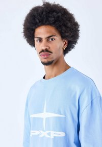 Lichtblauwe oversized t-shirt van katoen, met een groot wit grafisch ontwerp met tekst en steraccenten op de voorkant.