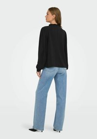 Svart långärmad blus med vågig halsringning, kombinerad med ljusblå vida jeans och svarta spetstövlar. Mjuk textur och avslappnad passform.