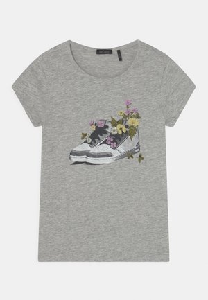 Camiseta de manga corta gris clara con una zapatilla estampada en blanco y negro, rellena de flores amarillas y moradas y hojas verdes.