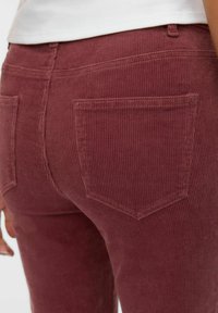 Pantalones de corduroy burdeos que presentan una textura acanalada, trabillas para cinturón y dos bolsillos traseros con un diseño clásico de costura.