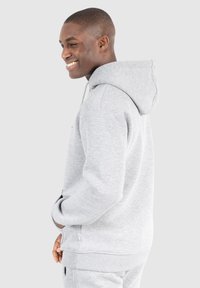 Grauer Hoodie mit Kapuze und Kordelzug, mit gerippten Bündchen und Saum. Hat eine glatte Textur und seitliche Taschen, kombiniert mit passenden grauen Hosen.