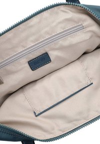 Tamsiai žalsvai mėlynos spalvos rankinės vidus su šviesiai rudos spalvos audinio pamušalu, užtrauktuku užsegama kišenė ir įmautės kišenė su tamsiai mėlynu ženkliuku. Minimalistinis dizainas.