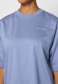 Jasnoniebieska koszulka z miękkiego materiału, z okrągłym dekoltem i krótkimi rękawami. Małe białe logo "Calvin Klein" na piersi.