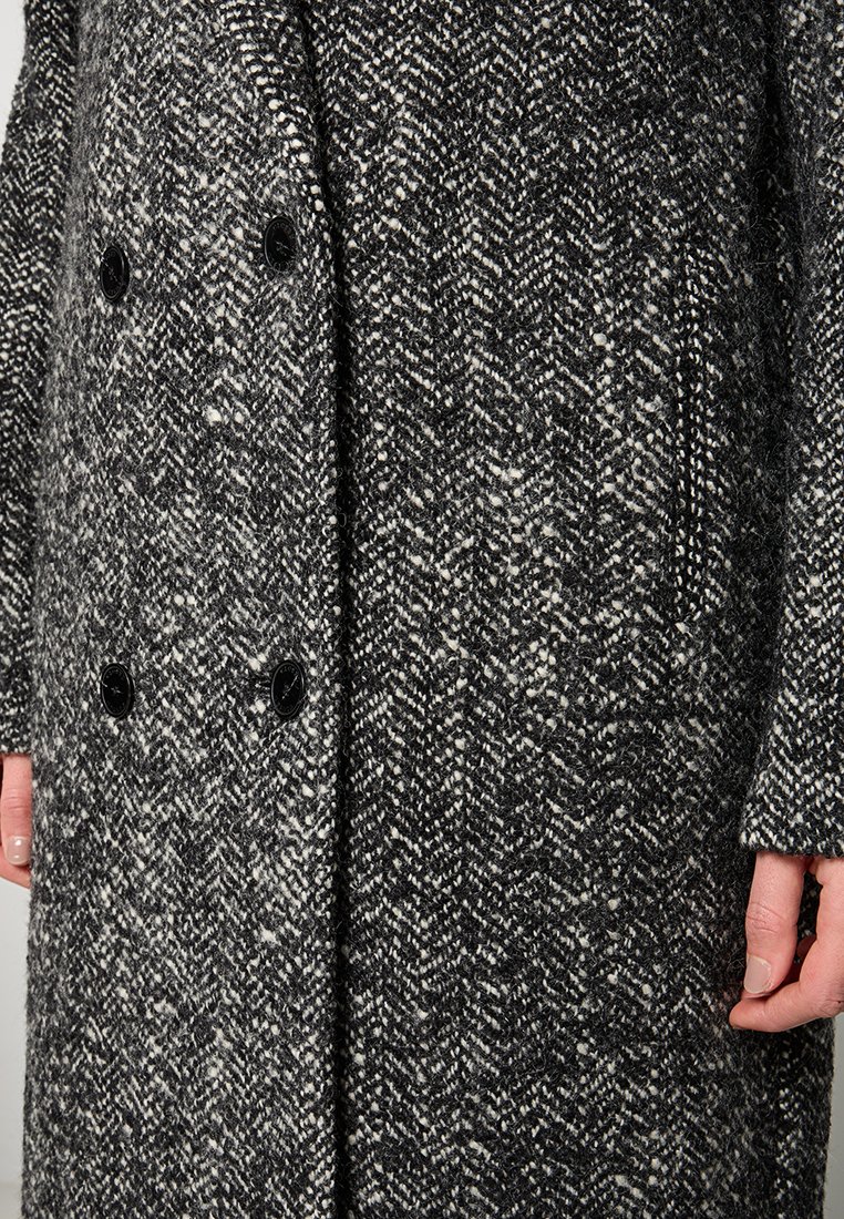 Dubbelzijdige jas in zwart-wit houndstoothpatroon, gemaakt van textuurstof met zwarte knopen en zijzakken.