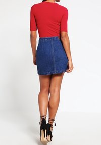 Červený žebrovaný top s krátkým rukávem v kombinaci s modrou džínsovou minisukní, která má vysoký pas a rovný střih, doplněná černými vysokými podpatky.
