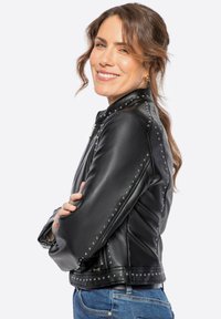 Black leather motorcycle jacket with studded accents along seams, fitted design, and zip closure. Smooth texture, cropped length.