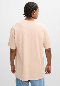 Camiseta corta de manga corta en rosa claro con un corte holgado y cuello redondo, confeccionada en suave material de algodón. Combinada con unos vaqueros de mezclilla azul claro.