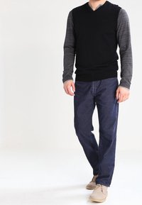 Svart V-ringad tröja med långa grå ärmar, kombinerad med mörkblå jeans och beige skor. Enkelt design, stickad textur på tröjan.