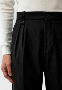 Zwarte broek met een op maat gemaakte snit, geplooide details, twee zwarte knopen aan de taille en een zachte stof. 