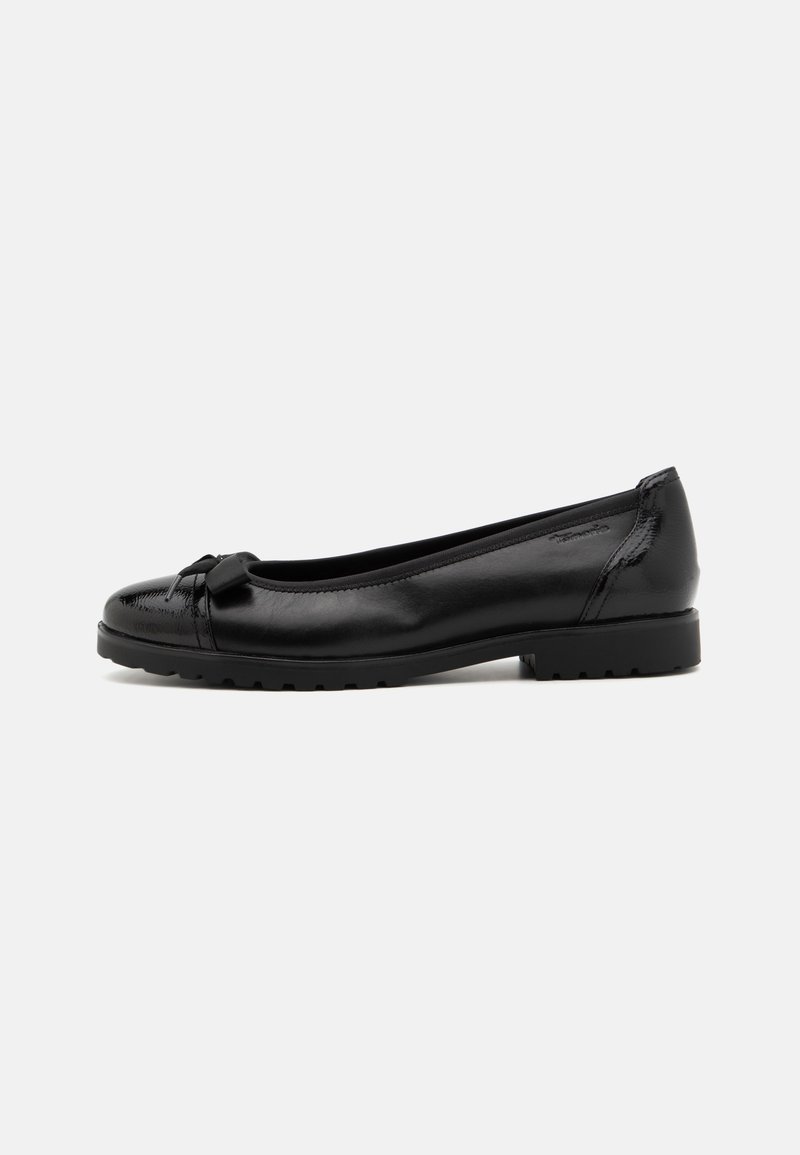 Chaussure plate en cuir noir avec bout rond, nœud décoratif et semelle épaisse en caoutchouc sur fond blanc uni.