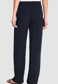 Donkerblauwe, wijde broek gemaakt van lichtgewicht stof. Voorzien van een elastische tailleband en twee achterzakken met subtiele branding.