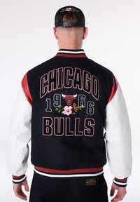 Black and white varsity jacket featuring red leather sleeves, embroidered "Chicago Bulls" text, floral accents, and ribbed cuffs.