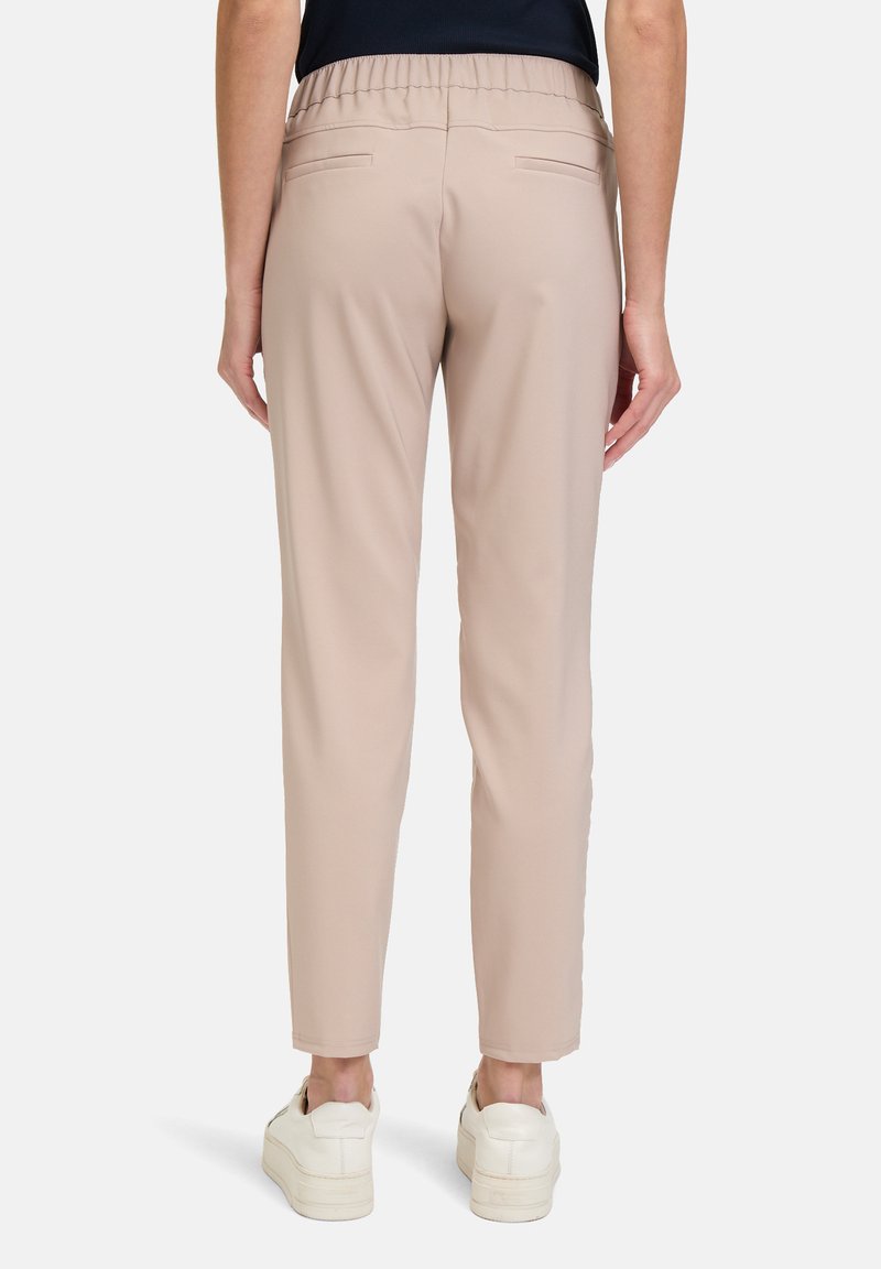 Beżowe tapered spodnie z elastycznym paskiem, dwiema tylnymi kieszeniami i miękkim, gładkim materiałem. Noszone z białymi trampkami.
