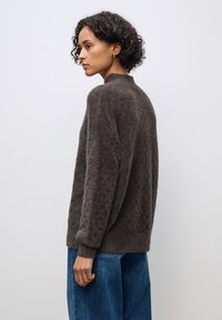 Maglione marrone e peloso con collo alto e maniche lunghe, dotato di una vestibilità rilassata. Abbinato a pantaloni in denim blu a gamba larga.
