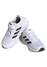 Zapatillas deportivas blancas con parte superior texturizada, que presentan tres rayas negras y una correa de velcro para un ajuste seguro. Punta redondeada y suela acolchada.