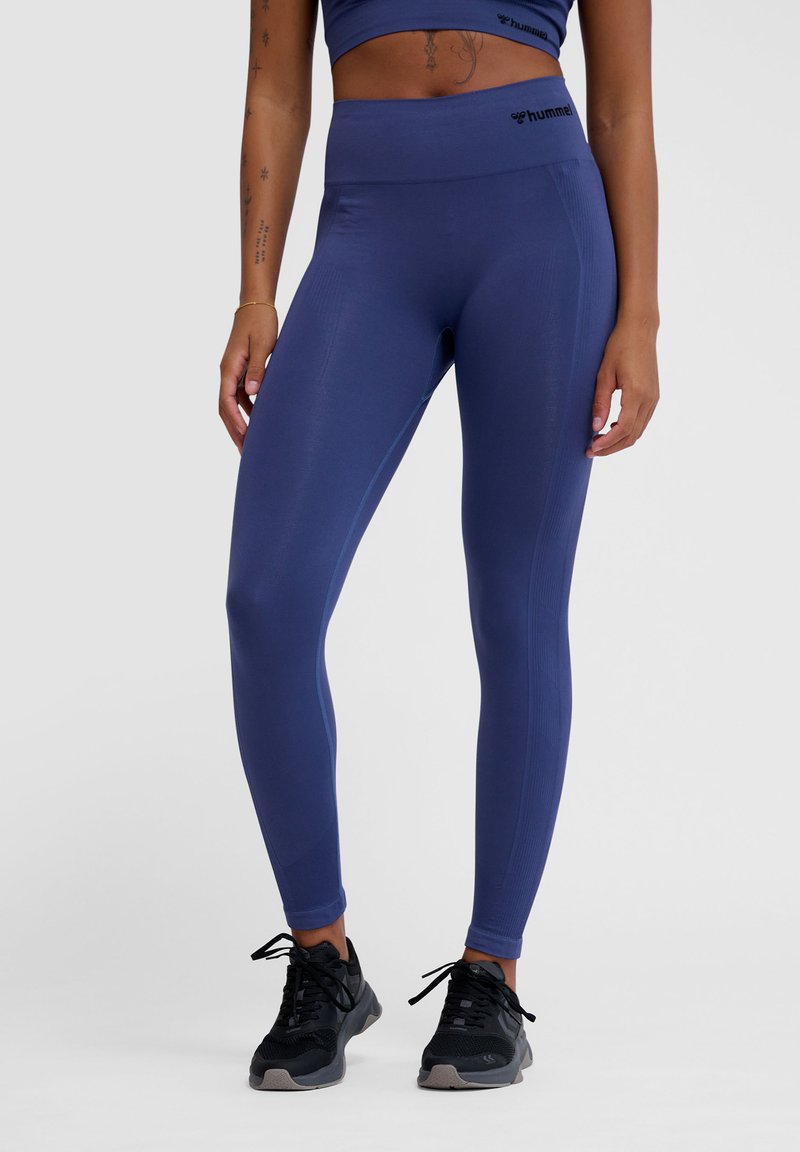 Marineblaue Stretch-Leggings mit hohem Bund und strukturierten Seitenelementen, kombiniert mit schwarzen Sportschuhen mit Schnürsenkeln und Polsterung.
