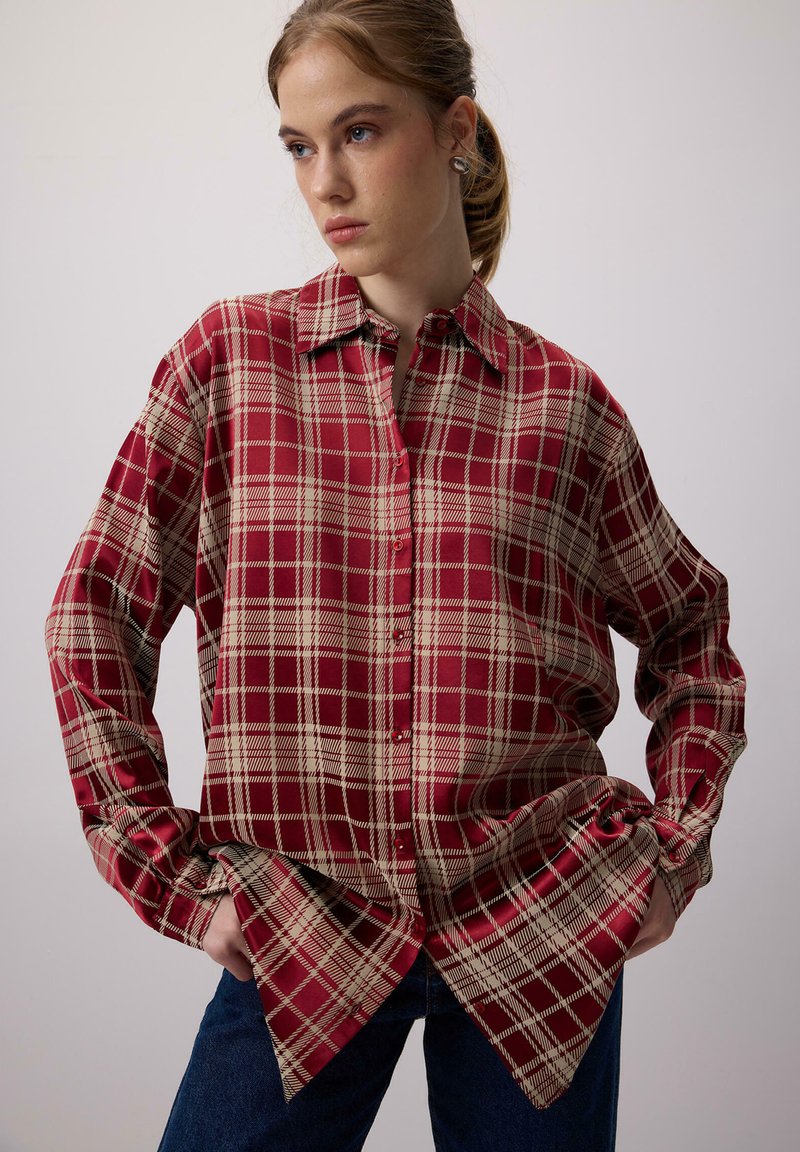 Punane ja beež kootud särk terava kaelusega, nööpidega ees, pikad varrukad ja laia lõikega. Kanga pind on sile ja läikiv.