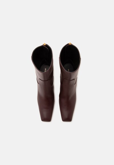 Paire de bottines en cuir marron foncé avec bouts carrés, vue de dessus sur un fond clair uni.