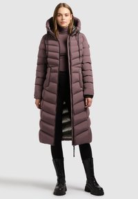 Garšs pūkains mētelis mīkstā maijās krāsā ar kapuci, ar šuvēm, priekšējo rāvējslēdzēju un vieglu iekšējo oderi. Uzvilkts virs melnajām biksēm un apaviem.