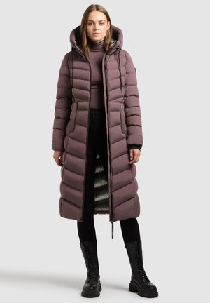 Cappotto lungo imbottito in morbido malva con cappuccio, caratterizzato da sezioni trapuntate, zip frontale e una fodera interna leggera. Indossato sopra pantaloni neri e stivali.