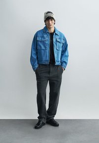 Τζιν μπουφάν σε ανοιχτό μπλε, με δύο μπροστινές τσέπες και χαλαρή εφαρμογή. Συνδυασμένο με μαύρες φόρμες και μαύρα αθλητικά παπούτσια. Περιλαμβάνεται πλεκτός σκούφος.