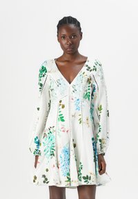 Abito floreale bianco con stampe botaniche verdi e blu, maniche lunghe a sbuffo, scollatura a V profonda e dettagli in pizzo lungo le cuciture.