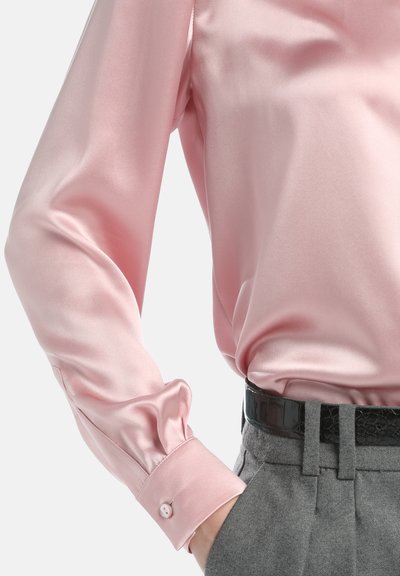 Rosa Satinbluse mit einem lockeren Schnitt, Knopfmanschetten und einer glatten Textur, kombiniert mit maßgeschneiderten grauen Hosen und einem schwarzen Gürtel.