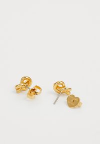 Gold-tone stud earrings featuring a twisted knot design with a textured finish and a heart-shaped tag engraved with "Kate Spade New York."