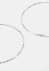 Boucles d'oreilles en argent en forme de créole, au design épuré et lisse. Elles présentent une forme circulaire continue et une texture fine et polie.