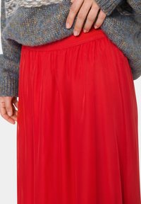 Falda roja y fluida con una pretina texturizada, hecha de tela ligera. La tela tiene un acabado liso y brillante, que se drapea de manera elegante.