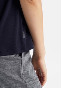 Maglietta a maniche corte blu navy realizzata in tessuto morbido, con un'etichetta sul lato. Abbinata a pantaloni corti sportivi grigio chiaro con un motivo testurizzato.