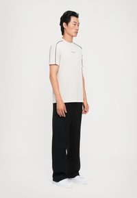 Camiseta gris claro con rayas negras en los hombros, combinada con pantalones negros de corte holgado y zapatillas blancas.