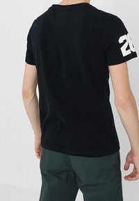 Černé bavlněné tričko s kulatým výstřihem a krátkými rukávy. Na zadní straně se nachází bílé číslo "28" na levém rukávu.