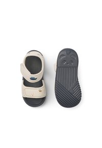 Μπεζ πρώτο παπούτσι με ρυθμιζόμενο λουράκι, ναυτικό μπλε σόλα, υφή στην επιφάνεια και διακοσμητικά σχέδια με βάρκα και μπάλα στο πάνω μέρος.