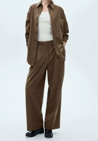 Chemise boutonnée marron à rayures fines avec une poche, associée à un pantalon large assorti. La tenue est complétée par des chaussures noires.