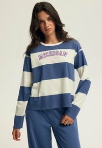 Niebieska i kremowa w paski koszula z długim rękawem z grafiką "MICHIGAN" w kolorze różowym. Miękka tkanina, luźny krój, okrągły dekolt, casualowy design.