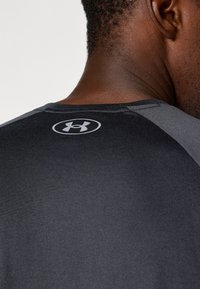 T-shirt de sport noir avec des accents gris, présentant une texture lisse et un design ajusté. Logo dans la partie supérieure du dos.